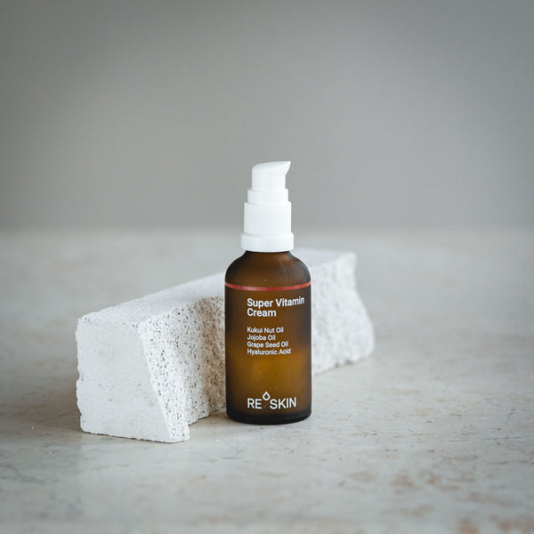 RE SKIN Super Vitamin Cream in einer braunen Pumpflasche neben einem hellen Steinblock.